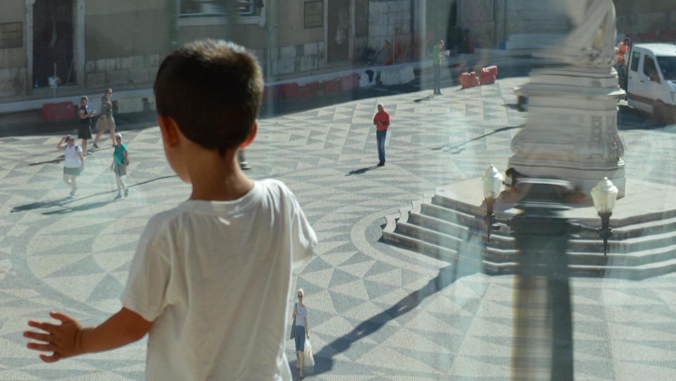 Criança de costa olha para a rua através de uma janela