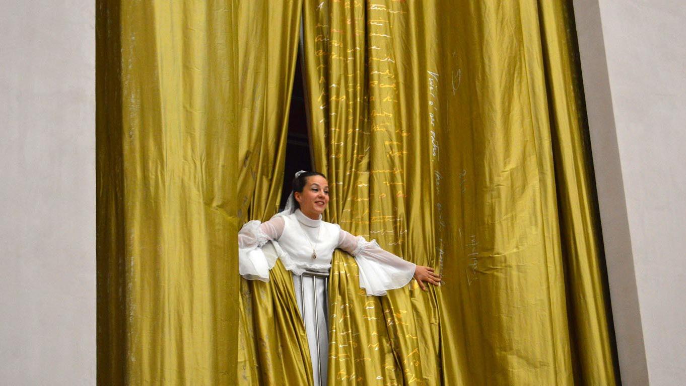 Atriz vestida de noiva espreita através das cortinas douradas
