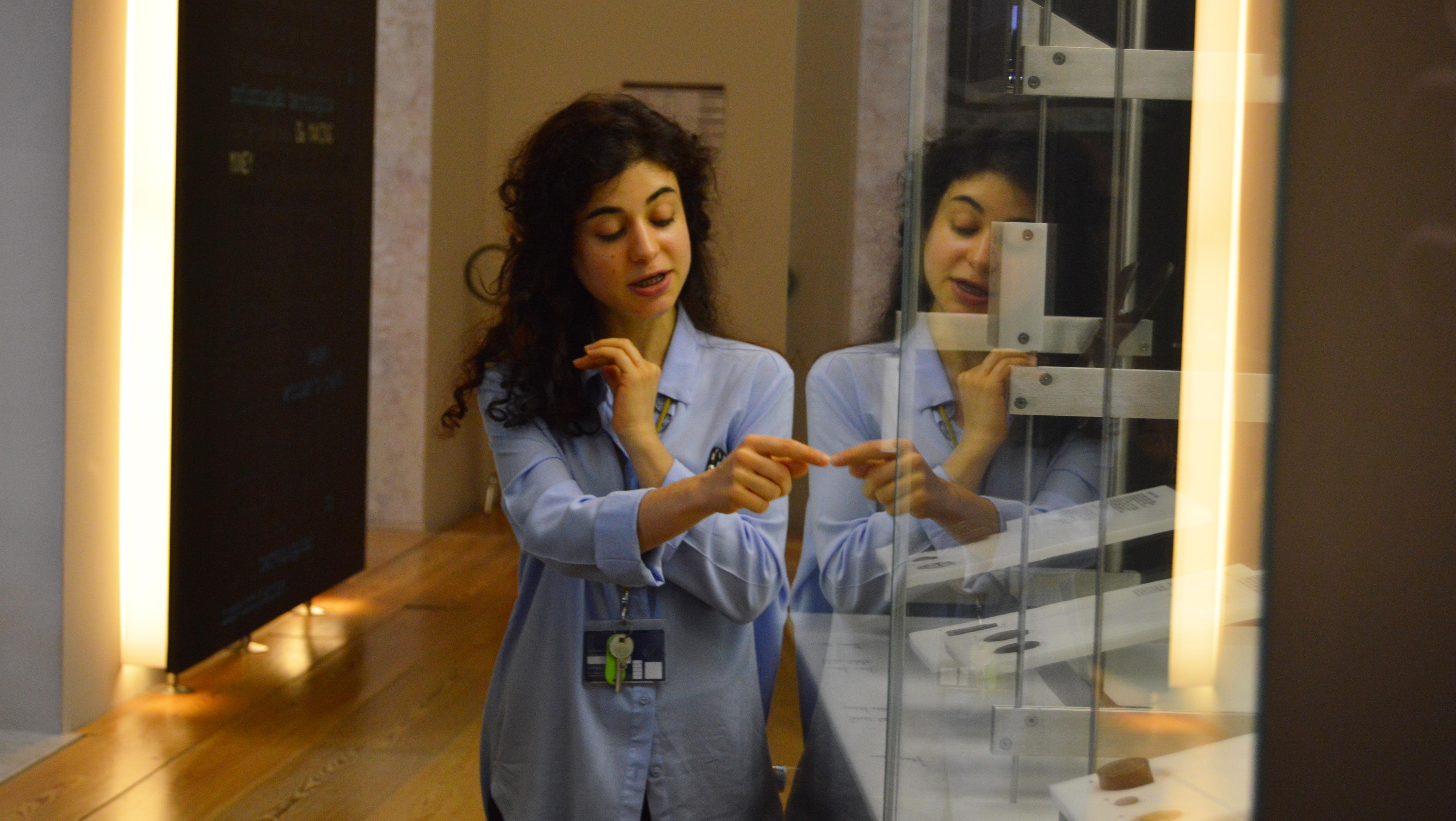 Pessoa aponta e fala sobre objecto dentro da vitrine