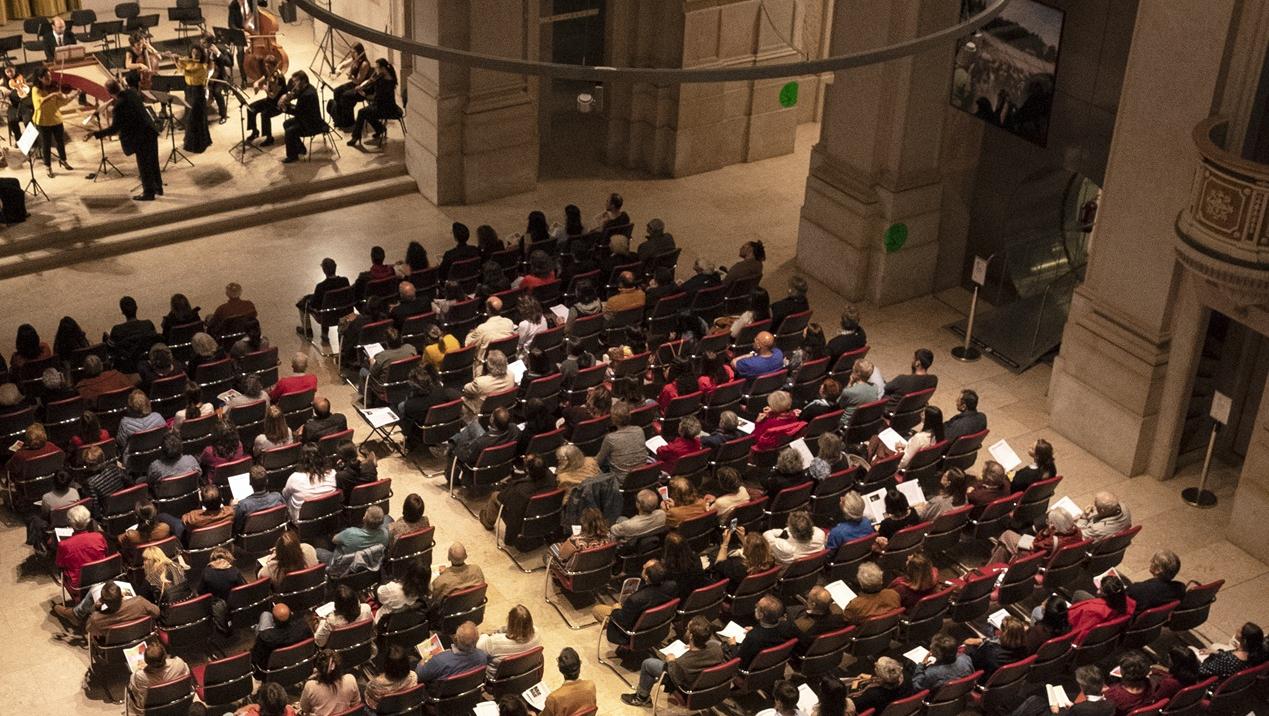 Pessoas sentadas na plateia assistem a um concerto