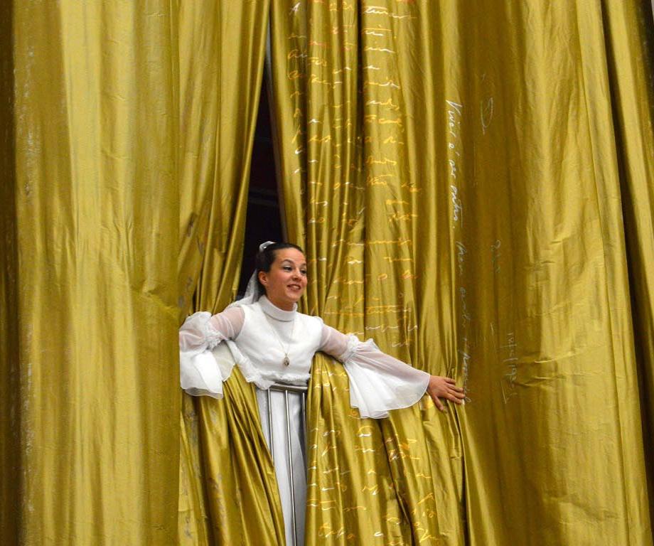 Atriz vestida de noiva espreita através das cortinas douradas 